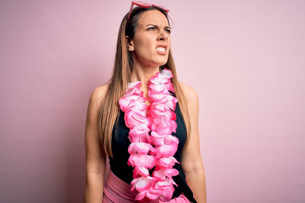 Young beautiful blonde woman wearing swimsuit and floral Hawaiian lei over pink background angry and mad screaming frustrated and furious, shouting with anger. Rage and aggressive concept. - Fotó, kép