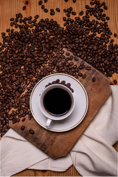 Café negro sobre fondo de madera rodeado de granos de café
 - Foto, Imagen