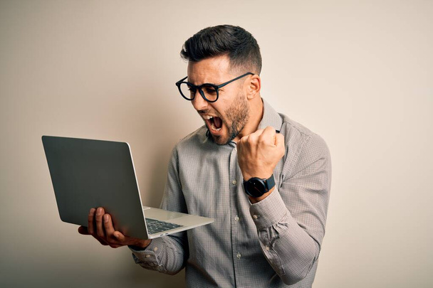 Fiatal üzletember visel szemüveget dolgozó számítógépes laptop bosszús és frusztrált kiabált harag, őrült és kiabál emelt kézzel, harag koncepció - Fotó, kép