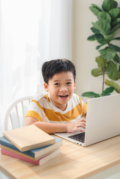 Azië tiener jongen studeren online op laptop met glimlachende en leuke gezicht thuis. Onlineonderwijs en e-learning. - Foto, afbeelding
