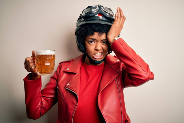 Young African American afro motorcyclist woman with curly hair drinking jar of beer stressed with hand on head, shocked with shame and surprise face, angry and frustrated. Fear and upset for mistake. - Photo, Image