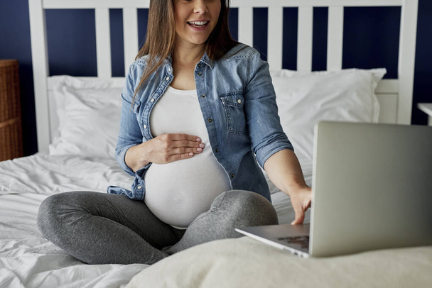 Nierozpoznawalna kobieta w ciąży korzystająca z laptopa w łóżku - Zdjęcie, obraz