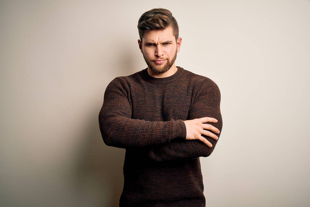 Young handsome blond man with beard and blue eyes wearing casual sweater standing skeptic and nervous, disapproving expression on face with crossed arms. Negative person. - Photo, Image