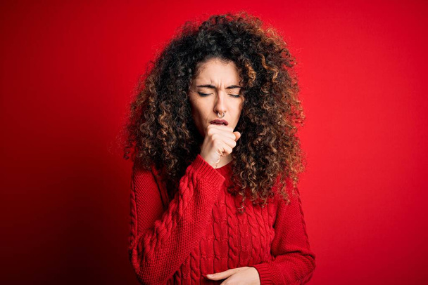 Fiatal gyönyörű nő göndör haj és piercing visel alkalmi piros pulóver rossz közérzet és köhögés tüneteként hideg vagy hörghurut. Egészségügyi koncepció. - Fotó, kép
