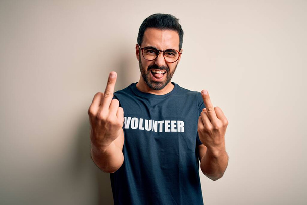 Красивий чоловік з бородою в футболці з волонтерським повідомленням на білому тлі Показує середній палець робить вам поганий вираз, провокації та грубе ставлення. Крик збуджений
 - Фото, зображення