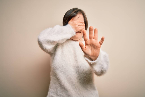 Young down syndrome woman standing over isolated background covering eyes with hands and doing stop gesture with sad and fear expression. Embarrassed and negative concept. - Photo, Image
