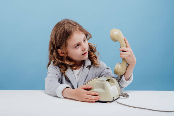 confused child girl with old telephone, sitting at the table, - Фото, изображение