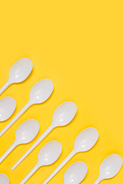 Disposable white plastic spoons on a yellow background - 写真・画像