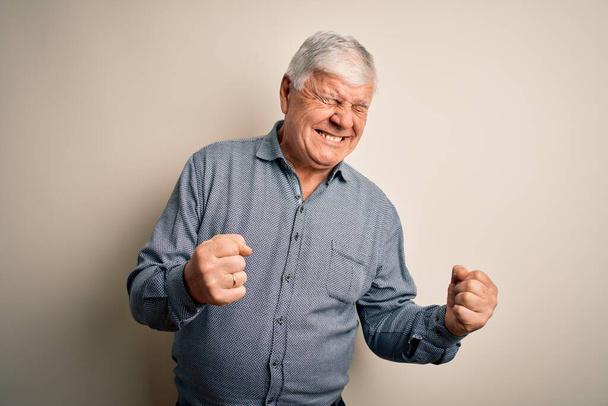 Senior handsome hoary man wearing casual shirt standing over isolated white background excited for success with arms raised and eyes closed celebrating victory smiling. Winner concept. - Foto, Imagen