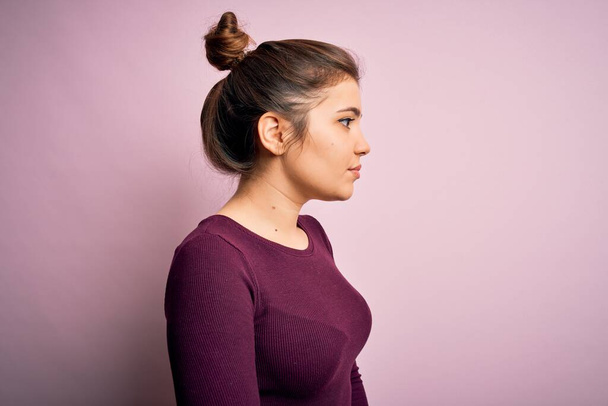 Beautiful young woman wearing casual bun hairstyle over pink isolated background looking to side, relax profile pose with natural face with confident smile. - 写真・画像