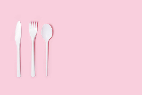 Disposable white plastic flatware on a pink background in a top view - Valokuva, kuva