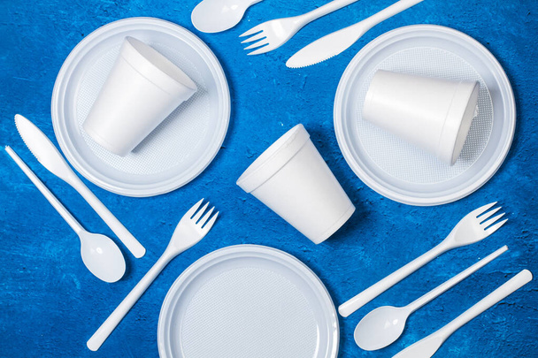 Disposable plastic white tableware on a textured classic blue background in a top view - Photo, Image