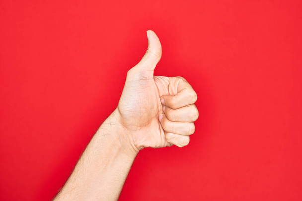 Hand of caucasian young man showing fingers over isolated red background doing successful approval gesture with thumbs up, validation and positive symbol - Фото, зображення