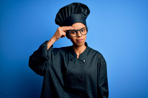 Nuori afrikkalainen kokki nainen yllään liesi univormu ja hattu sinisellä taustalla huolissaan ja korosti ongelmaa käsi otsassa, hermostunut ja ahdistunut kriisistä
 - Valokuva, kuva
