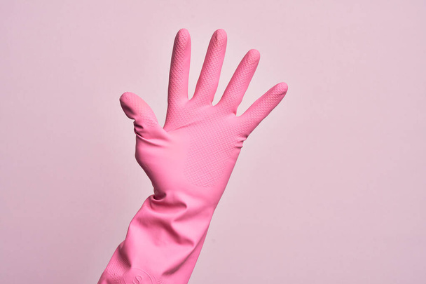 Hand van blanke jongeman met reinigingshandschoen over geïsoleerde roze achtergrond tellen nummer 5 met vijf vingers - Foto, afbeelding