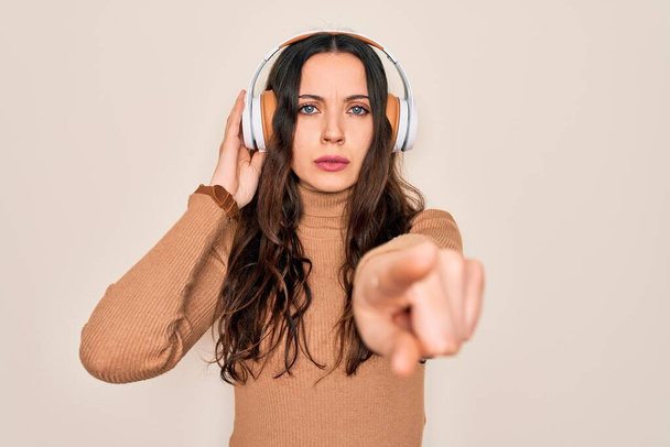 Young beautiful woman with blue eyes listening to music and dancing using headphones pointing with finger to the camera and to you, hand sign, positive and confident gesture from the front - 写真・画像