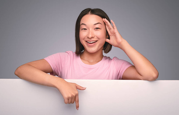 Onnellinen aasialainen nainen osoittaa juliste
 - Valokuva, kuva