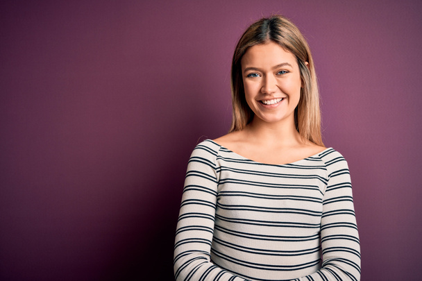 Young beautiful blonde woman wearing casual striped shirt over purple isolated background with a happy and cool smile on face. Lucky person. - Photo, Image