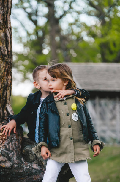 Porträt des kleinen Bruders und der kleinen Schwester, die neben dem alten Baumstamm stehen und sich umarmen und zur Seite schauen - Foto, Bild