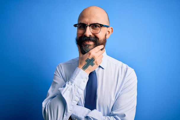 Handsome business bald man with beard wearing elegant tie and glasses over blue background looking confident at the camera smiling with crossed arms and hand raised on chin. Thinking positive. - Фото, зображення