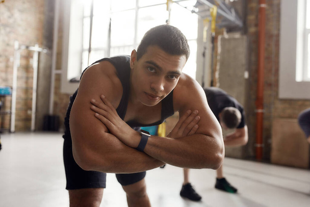 Get stronger. Portrait of athletic man in sportswear looking at camera, stretching his body while working out in industrial gym. Group training concept - Photo, image