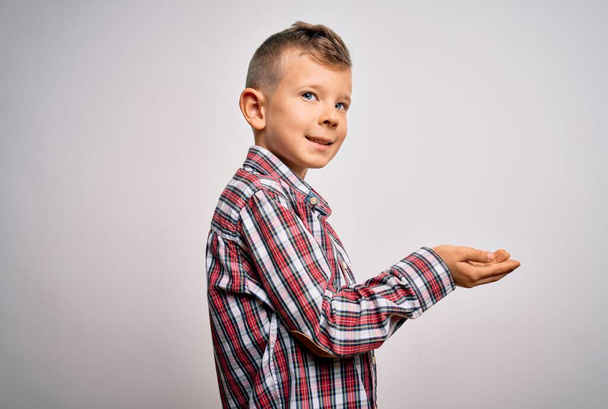 Young little caucasian kid with blue eyes wearing elegant shirt standing over isolated background pointing aside with hands open palms showing copy space, presenting advertisement smiling excited happy - Foto, Imagen