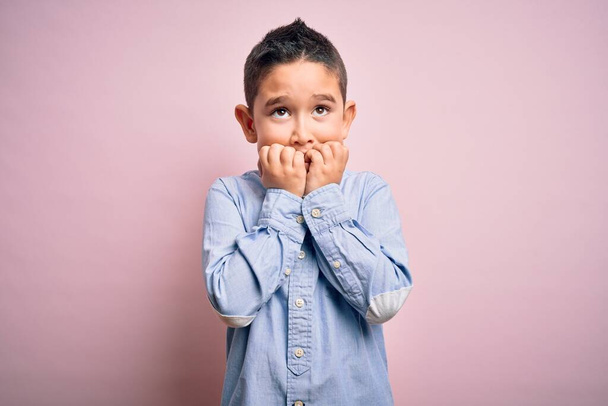 Jeune garçon enfant portant une chemise élégante debout sur fond rose isolé regardant stressé et nerveux avec les mains sur les ongles mordants de la bouche. Problème d'anxiété
. - Photo, image