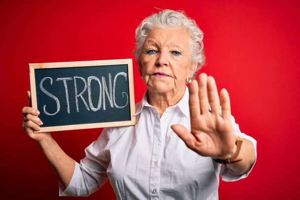 Senior beautiful woman holding blackboard with strong message over isolated red background with open hand doing stop sign with serious and confident expression, defense gesture - Photo, Image