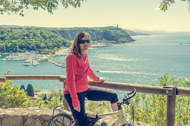 自転車で休息し、素晴らしい海の景色を楽しむアクティブな女性サイクリスト. - 写真・画像