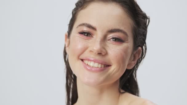 A close-up view of a cheerful happy young half-naked woman with wet hair is laughing to the camera isolated over a light blue background in studio - Materiał filmowy, wideo