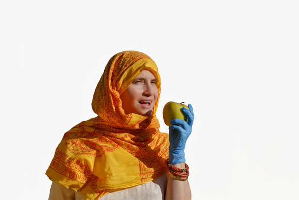 Portrait of a woman in Indian dress and blue protective gloves biting an apple - Foto, Bild