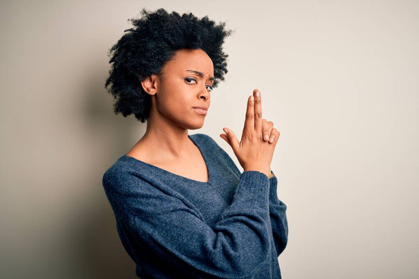 Jonge mooie Afro-Amerikaanse afro vrouw met krullend haar dragen casual trui Holding symbolische pistool met de hand gebaar, het spelen van het doden van wapens, boos gezicht - Foto, afbeelding