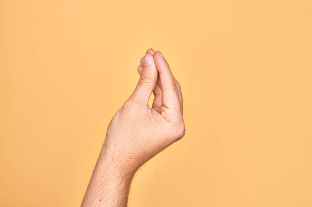 Mano de joven caucásico mostrando los dedos sobre fondo amarillo aislado haciendo gesto italiano con los dedos juntos, movimiento de gesto de comunicación - Foto, imagen