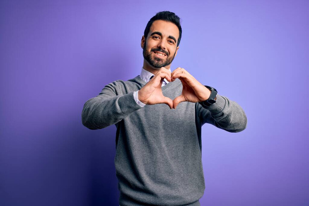 Handsome businessman with beard wearing casual tie standing over purple background smiling in love doing heart symbol shape with hands. Romantic concept. - Photo, Image