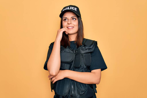 Молода красива брюнетка поліцейська в уніформі поліції куленепробивна і шапка з рукою на підборідді думає про питання, стомлювальне вираження. Усміхнене і вдумливе обличчя. Концепція сумніву
. - Фото, зображення