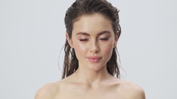 A charming young half-naked woman with wet hair is posing with a powder brush isolated over a light blue background in studio - Materiał filmowy, wideo