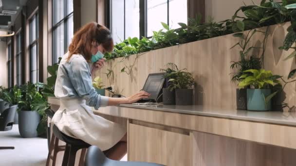 Nő visel higiénikus maszk és köhögés használata közben laptop dolgozni a munkahelyen. - Felvétel, videó