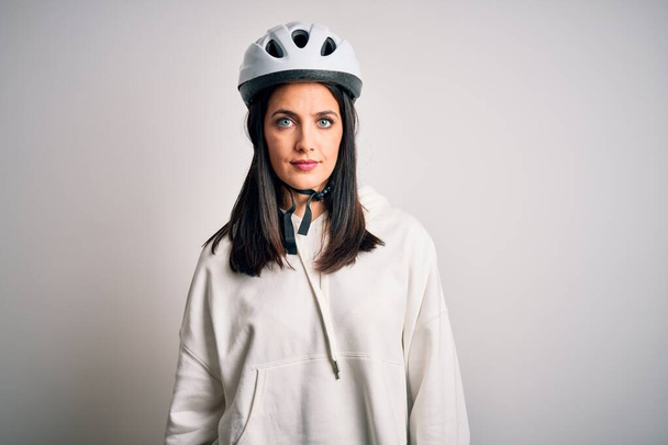 Mavi gözlü genç bisikletçi kadın izole edilmiş beyaz arka planda bisiklet kaskı takıyor ve yüzünde ciddi bir ifade var. Basit ve doğal bir şekilde kameraya bakıyorsun.. - Fotoğraf, Görsel