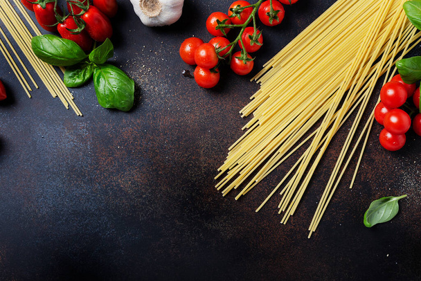 Ingredients for cooking italian pasta: spaghetti, tomato, basil and garlic on the black table. Top view image with a copy space - Foto, afbeelding