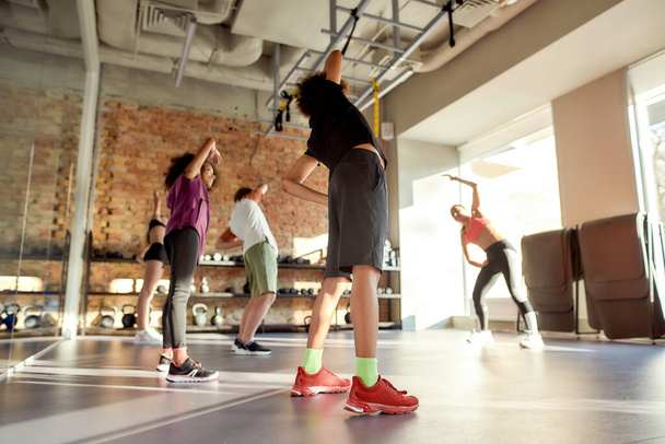 Celebrating health. Full-length shot of a boy warming up, exercising together with other kids and female trainer in gym. Sport, healthy lifestyle, active childhood concept - Photo, Image