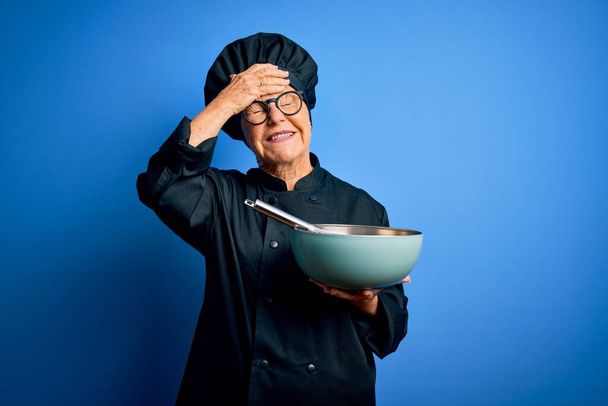 Senior beautiful grey-haired chef woman wearing cooker uniform and hat using whisk and bowl stressed with hand on head, shocked with shame and surprise face, angry and frustrated. Fear and upset for mistake. - Photo, Image