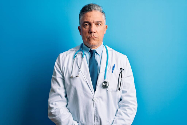 Pohledný šedovlasý lékař středního věku v kabátě a modrém stetoskopu Uvolněný s vážným výrazem ve tváři. Jednoduchý a přirozený pohled do kamery. - Fotografie, Obrázek