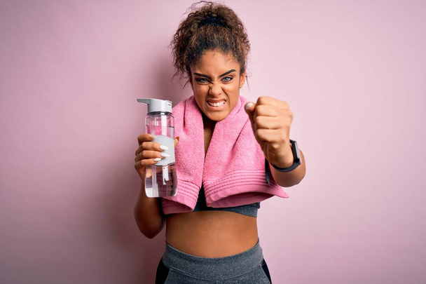Young african american sporty girl doing sport wearing towel drinking bottle of water annoyed and frustrated shouting with anger, crazy and yelling with raised hand, anger concept - Zdjęcie, obraz