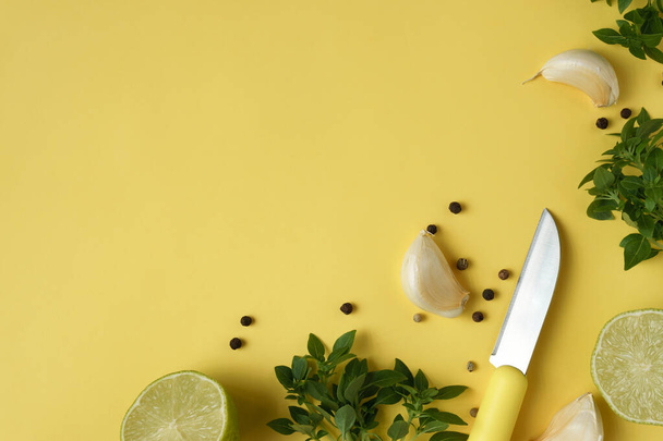 Basilico, grani di pepe, spicchi d'aglio, lime, coltello da cucina su fondo giallo
 - Foto, immagini
