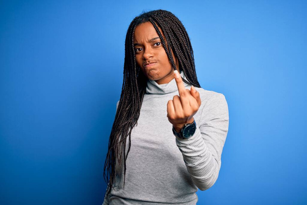 Young african american woman standing wearing casual turtleneck over blue isolated background Showing middle finger, impolite and rude fuck off expression - Photo, Image