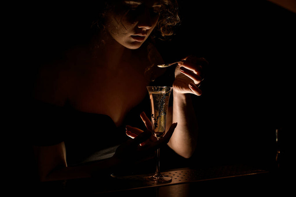 attractive girl at dark bar holds teaspoon over glass with cocktail - Fotoğraf, Görsel