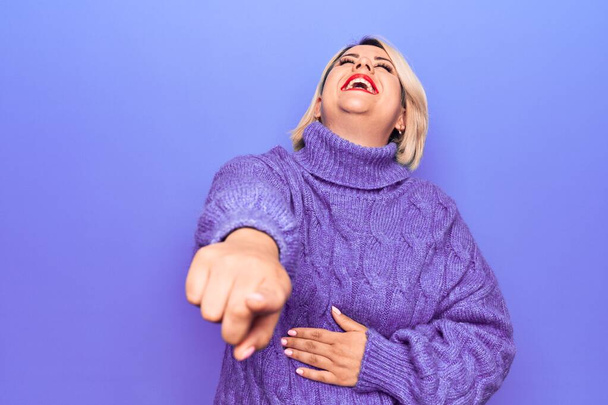 Bella bionda plus size donna indossa casual maglione dolcevita su sfondo viola ridere di te, puntando il dito verso la fotocamera con mano sul corpo, espressione di vergogna - Foto, immagini