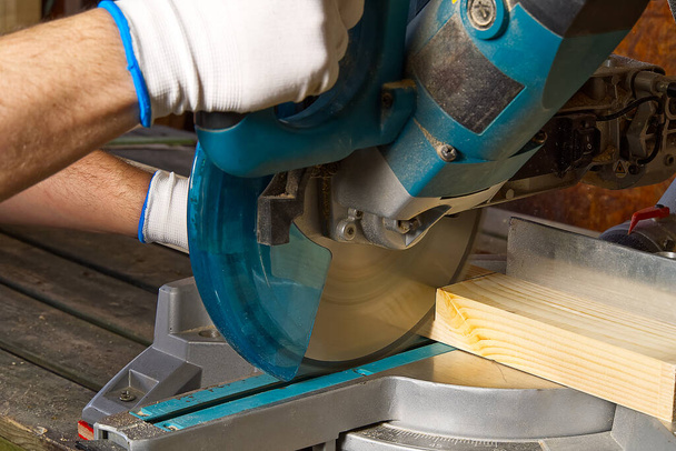 Detailní záběr profesionálních skříňkářů pracujících s elektrickou kruhovou pilou na dřevoobráběcí dílně. Kvalifikovaný tesař řeže dřevěnou desku kulatou pilou. Výroba dřevěného materiálu. Dřevařská továrna - Fotografie, Obrázek