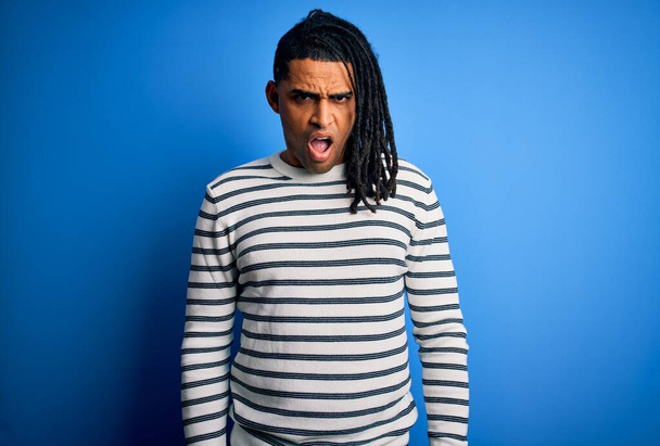 Joven guapo afroamericano afro hombre con rastas vistiendo suéter de rayas casuales En la cara de choque, mirando escéptico y sarcástico, sorprendido con la boca abierta
 - Foto, imagen