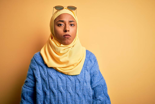 Nuori afroamerikkalainen opiskelija nainen yllään keltainen muslimi hijab ja aurinkolasit vakava ilme kasvoilla. Yksinkertainen ja luonnollinen kameraan katsominen
. - Valokuva, kuva